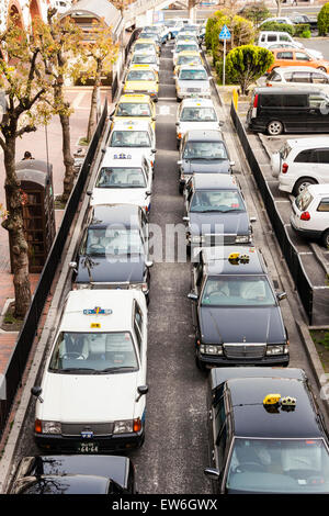 Vue en hauteur de la double rangée de taxis qui attendent sur la route, des taxis jaunes, noirs et blancs à l'extérieur de la gare (non représentés) , à Kurashiki au Japon. Banque D'Images