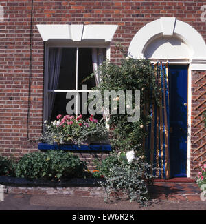 De l'extérieur d'un petit duplex de géraniums roses dans la fenêtre de dialogue et un rideau en toile sur la porte avant Banque D'Images