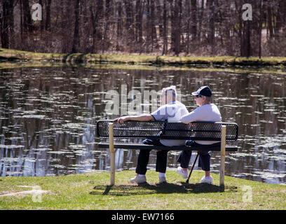 Vieux couple assis sur un banc à côté d'un étang Banque D'Images