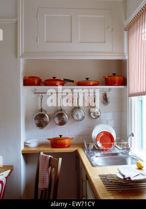 Rangée de casseroles Le Creuset orange sur l'étagère au-dessus des casseroles en acier inoxydable sur rack dans cuisine blanche Banque D'Images