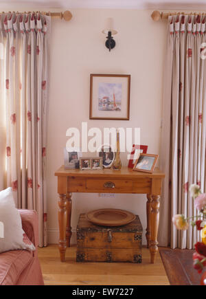 Vieille boîte en bois ci-dessous petite table en pin entre fenêtres avec rideaux blancs à motifs rouge dans le pays de séjour Banque D'Images