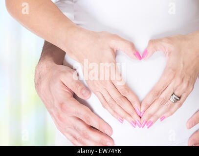 Photo gros plan de la femme enceinte et son mari se tenant la main sur le ventre en forme de coeur, de bonheur et de santé pour la grossesse Banque D'Images