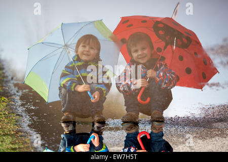 Deux petits garçons, l'accroupissement sur une flaque d'eau, avec peu de parasols Banque D'Images