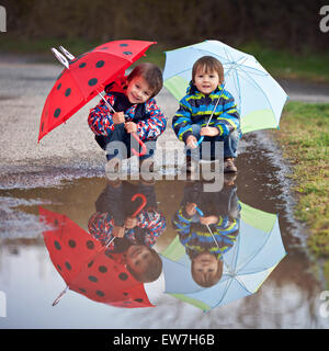 Deux petits garçons, l'accroupissement sur une flaque d'eau, avec peu de parasols Banque D'Images