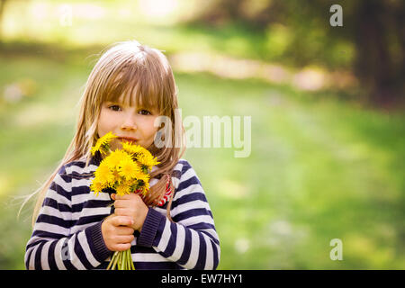 Belle petite fille blonde, à l'outdoor,holding bouquet de pissenlits, printemps, la fin de l'après-midi ensoleillé Banque D'Images