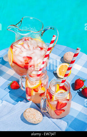 Froid de glace limonade aux fraises faites maison en pichet et verres avec paille de papier sur la table à côté de la piscine extérieure d'été Banque D'Images