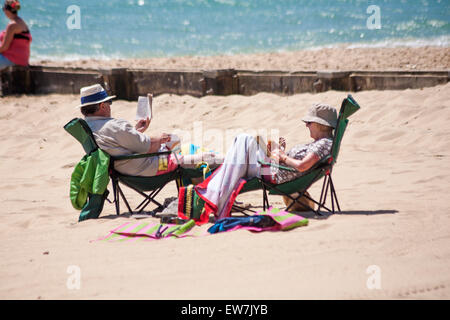 Bournemouth, Dorset, UK 19 juin 2015. Couple assis sur des chaises de la lecture des livres de poche et de manger sur une chaude journée ensoleillée à la plage de Bournemouth Crédit : Carolyn Jenkins/Alamy Live News Banque D'Images