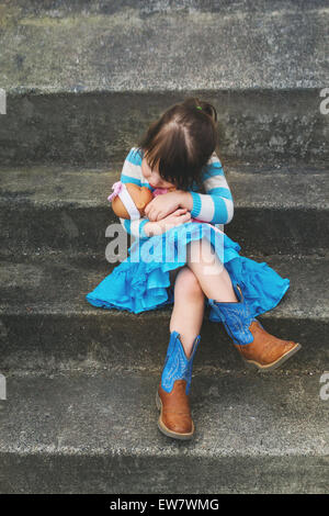 Fille assise sur une étape hugging a baby doll Banque D'Images