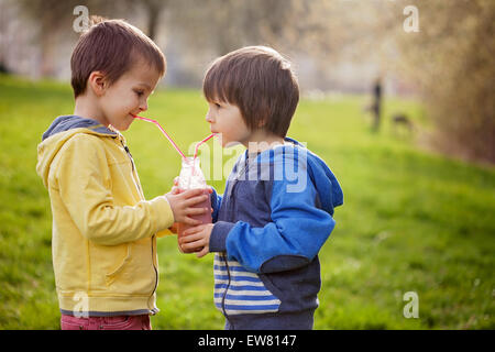 Les garçons doux dans le parc, tenant la bouteille de smoothie, boisson et souriant, le printemps Banque D'Images