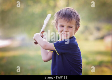 Petit garçon en colère, tenant un sabre, avec un fou face à l'appareil photo, à l'extérieur dans le parc Banque D'Images