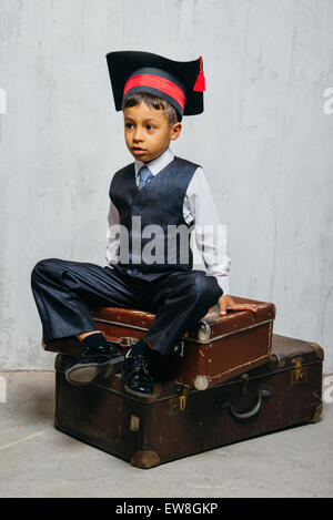 Petit garçon noir en graduation hat se trouve sur l'ancienne valises Banque D'Images