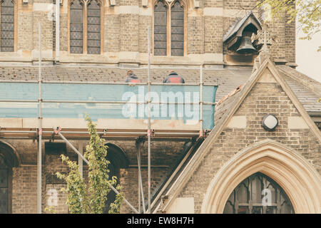 La réparation des constructeurs de toit une église debout sur les échafaudages, l'église en arrière-plan Banque D'Images