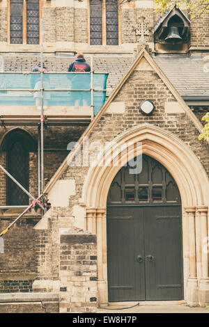 La réparation des constructeurs de toit une église debout sur des échafaudages, porte de l'église en premier plan Banque D'Images