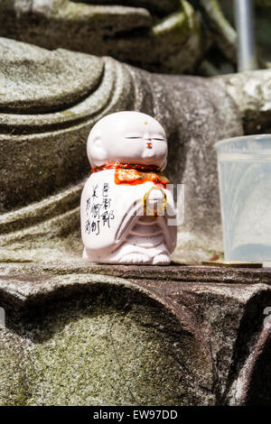 Le Japon, l'Onomichi, Temple Senkoji. Un petit Ojizo-sama, jizo Jizo bosatsu, figure avec dossard rouge, à gauche à la base d'une statue de l'un des dieux japonais. Banque D'Images