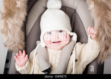 Drôle de petit bébé dans un chapeau chaud assis dans une poussette Banque D'Images