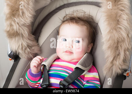 Magnifique petite fille dans une robe en tricot rose assis dans une poussette Banque D'Images