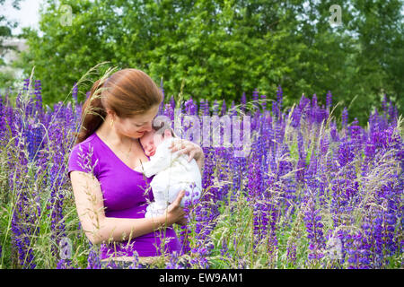 Jeune mère tenant son bébé nouveau-né dans un champ de fleurs de mauve Banque D'Images