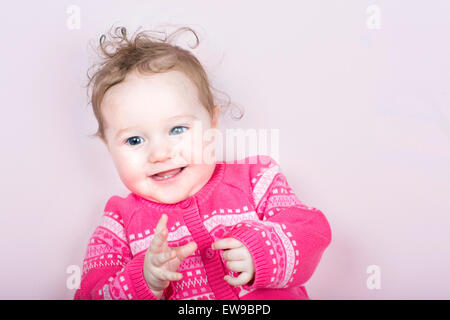 Cute baby girl in a pink chandail tricoté avec des cœurs sur une couverture rose Banque D'Images