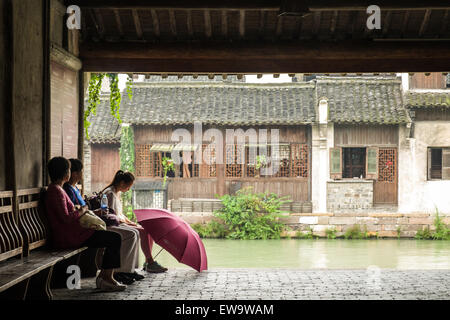 Personnes assises sur un banc sous le toit le long d'un canal dans la pittoresque ville aquatique historique de Wuzhen, en Chine Banque D'Images