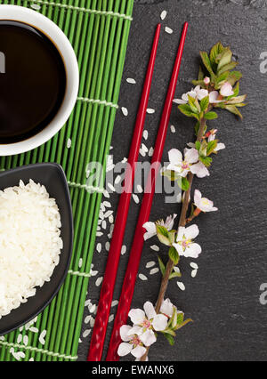 Les sushis japonais Les baguettes, bol de sauce de soja, de riz et de sakura en fleurs sur fond noir en noir Banque D'Images