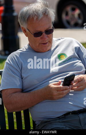 Senior male assis dans le soleil des messages sur son téléphone cellulaire Banque D'Images