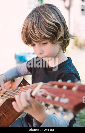 Petit garçon blond jouant de la guitare espagnole à l'extérieur Banque D'Images