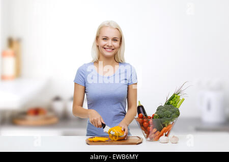 Souriante jeune femme hacher les légumes sur la cuisine Banque D'Images