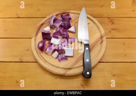 Oignon rouge haché avec un couteau de cuisine sur une planche sur une table en bois Banque D'Images