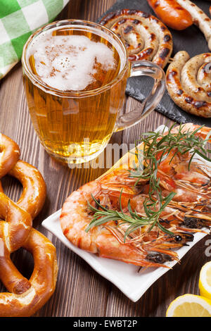 Beer mug, crevettes grillées, saucisses et bretzels sur table en bois Banque D'Images