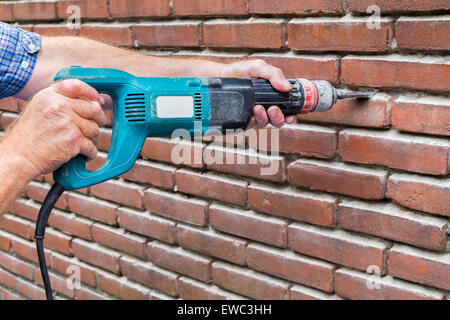 Armoiries de construction worker holding machine de forage contre brick wall Banque D'Images