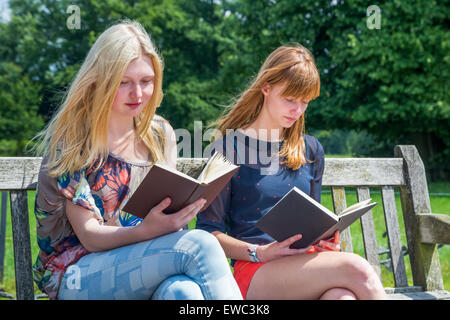 Deux adolescentes de race blanche à lire des livres sur un banc dans la nature verte Banque D'Images