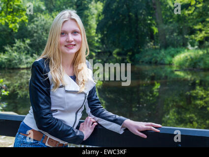 Blond caucasian teenage girl leaning on fence près de l'eau de l'étang en forêt Banque D'Images