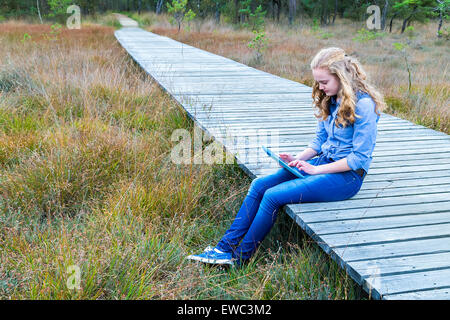 Blond caucasian teenage girl travailler avec tablet computer on wooden path dans la nature Banque D'Images