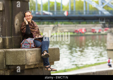 Woman with laptop sitting outdoors à parler au téléphone. Banque D'Images