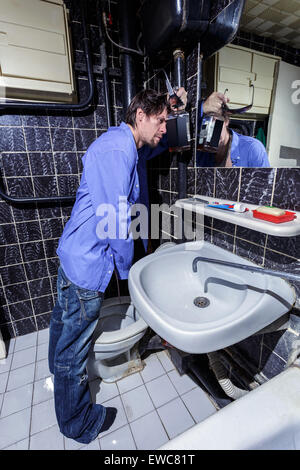 L'homme ivre est debout dans une salle de bain avec une bouteille de whisky, image en couleur Banque D'Images