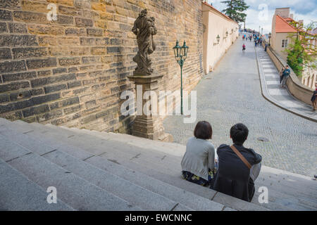 Jeunes assis seuls, vue d'un jeune couple assis seul sur des marches et regardant vers l'approche élevée du château de Prague, République tchèque Banque D'Images
