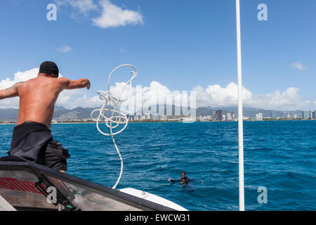 Un homme jette une corde à un plongeur d'ancrer un bateau de plongée à une amarre de ballon sur la plage de Waikiki à plonger. Banque D'Images