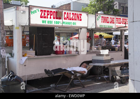 Vendeur alimentaire prend une sieste derrière sa concession à un festival de rue le long de Flatbush Avenue à Brooklyn, New York. Banque D'Images