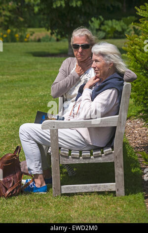 Deux femmes âgées assis sur un banc et détendue le soleil brille à Dorset en Juin Banque D'Images