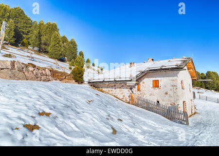 Chalet alpin entouré par une clôture dans la neige entre les sommets enneigés et les forêts de pins sur une journée ensoleillée en hiver Banque D'Images