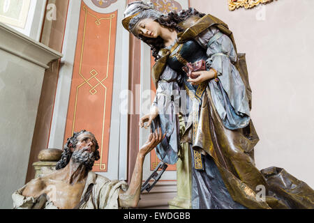 Bois sculpté statue de Saint Elizabeth donnant une pièce de monnaie avec sa main droite à la main gauche de mendiant comme geste de charité Banque D'Images