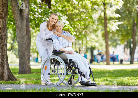 Jeunes femmes en uniforme avec senior patient in a wheelchair chilling out in park Banque D'Images