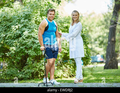 Happy nurse soutenir jeune homme avec walker alors que tous les deux à l'extérieur de l'appareil photo Banque D'Images