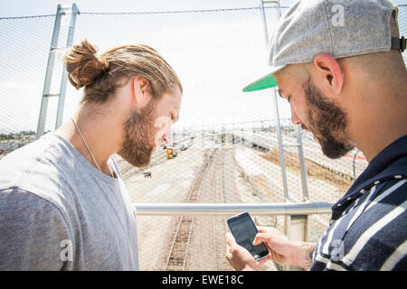 Deux jeunes hommes se tenant debout sur la passerelle looking at mobile phone Banque D'Images