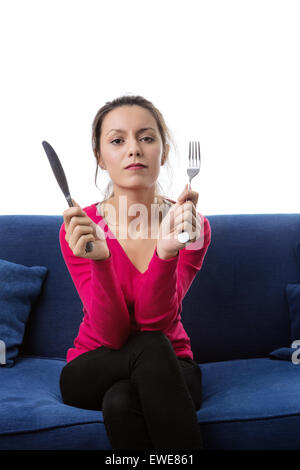 Femme assise sur un canapé avec une fourchette et couteau en attente de son dîner Banque D'Images