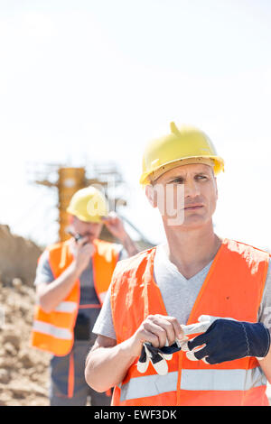 Thoughtful worker at construction site with colleague in background Banque D'Images