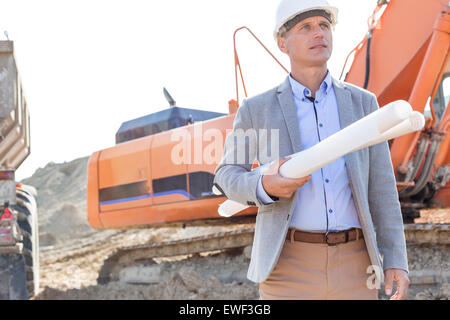 Architecte confiant à la voiture tandis que holding blueprints at construction site Banque D'Images