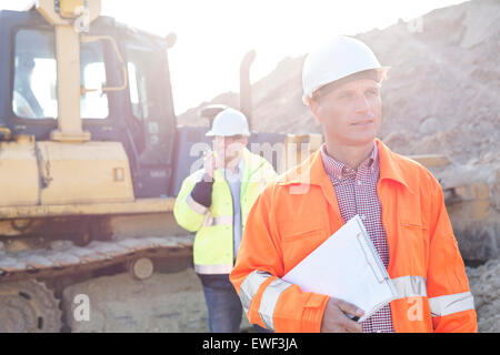 Holding clipboard ingénieur sur site de construction avec un collègue en arrière-plan Banque D'Images