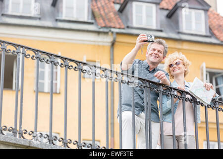 Happy middle-aged couple en tenant l'appareil photo numérique par selfies contre le bâtiment Banque D'Images