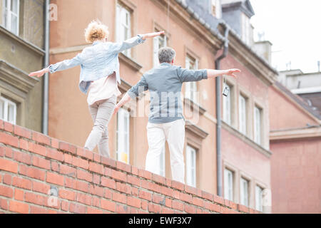 Vue arrière du couple with arms outstretched marcher sur mur de brique Banque D'Images